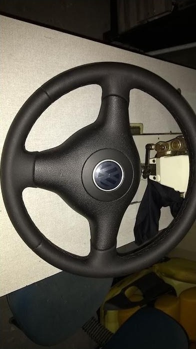 Volante revestido em couro preto, pendurado na oficina com a máquina de costura ao fundo